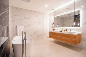A modern bathroom with a marble wall, a freestanding bathtub, a wooden vanity, and pendant lights. - AR Villa Sayan (Ubud)