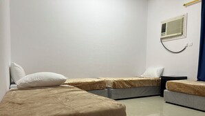 A room with two beds, each with a pillow and a blanket. There is a small table and a wall-mounted heater. - Jawar Al Rahma (Madinah)