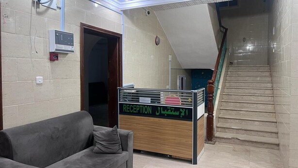 A reception area with a reception desk, a grey sofa, and a staircase leading to an upper floor. - Jawar Al Rahma (Madinah)