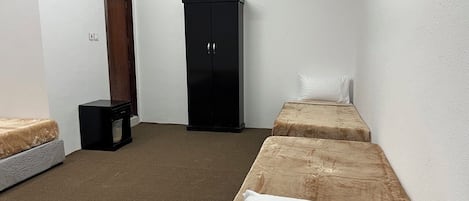A small, sparsely furnished room with two single beds, a wardrobe, and a heater.