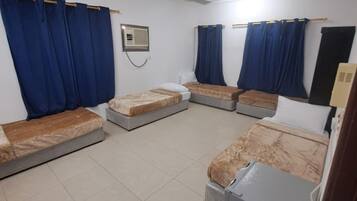Een kamer met vier eenpersoonsbedden, een plafondventilator en een heater.