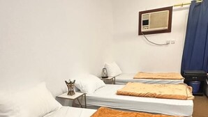A hotel room with three beds, each with white bedding and a brown throw blanket. There is a small table with a lamp and a decorative item on it. A television is mounted on the wall above the beds. - Jawar Al Rahma (Madinah)
