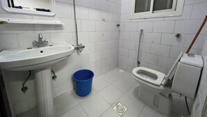 A small, basic bathroom with a white sink, a toilet, and a blue bucket. - Jawar Al Rahma (Madinah)