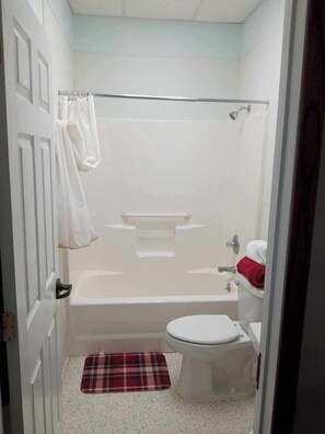A small bathroom with a shower, toilet, and a red plaid bath mat.
