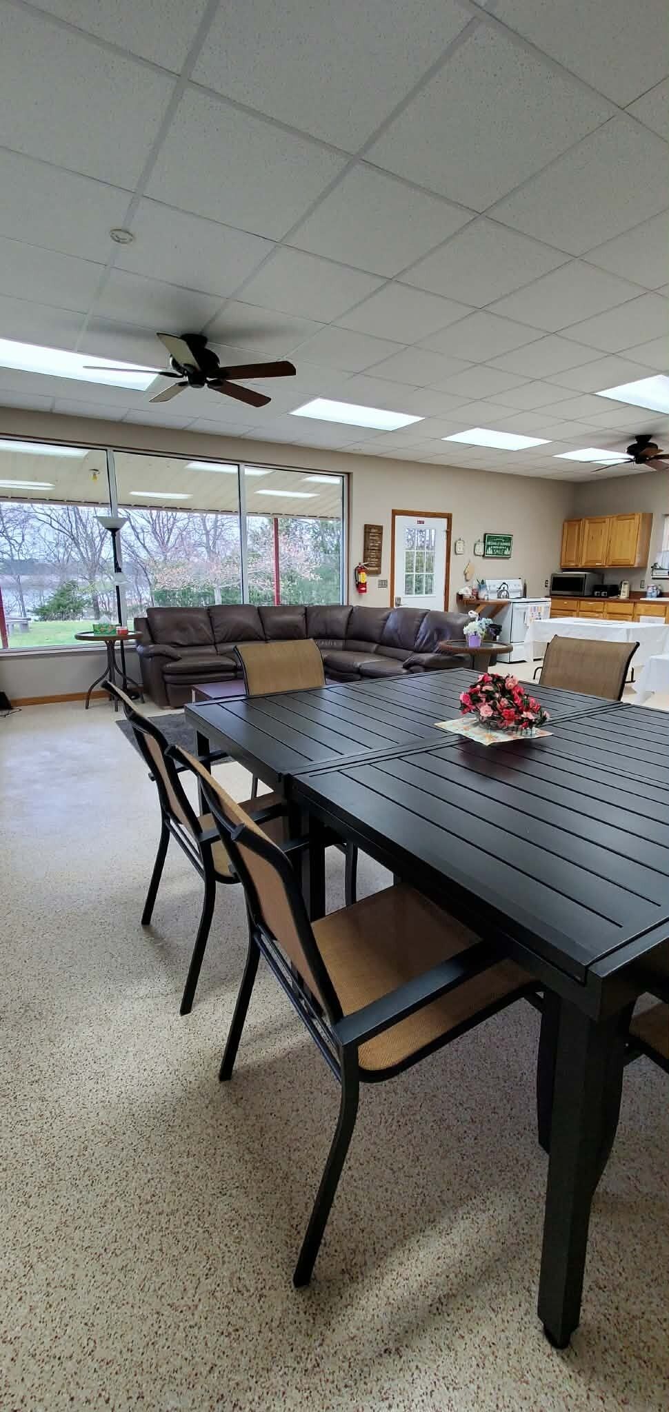 A conference room with a long table, chairs, a ceiling fan, and a view of the outdoors.