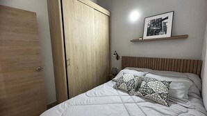 Un dormitorio con cama, armario, mesita de noche, lámpara y un cuadro en la pared.