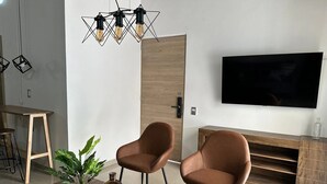 Una sala moderna con dos sillones de cuero marrón, una mesa de centro de madera con una planta, un televisor en la pared y una puerta de madera.