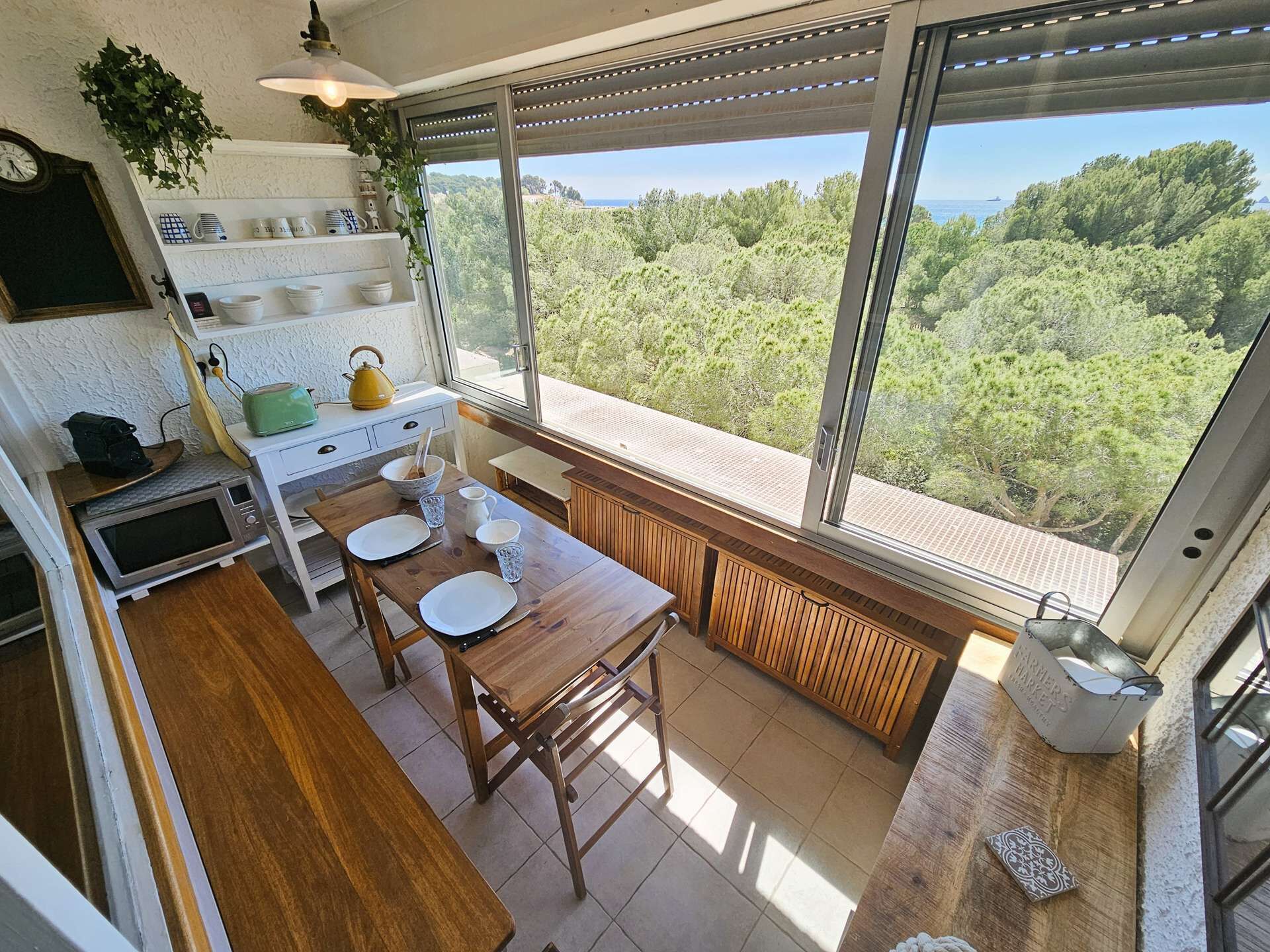 A kitchen with a wooden table, white plates, and a view of a forest through large windows.