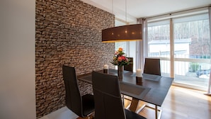A modern dining area with a stone wall, a table with chairs, a vase with flowers, and large windows with a view of the outdoors. - Ocean Club - Exklusive Ferienwohnung: mit Balkon, Direktem Ostseeblick & Strandzugang (Timmendorfer Strand)