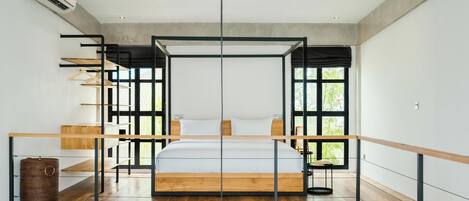 Une chambre moderne avec un grand lit, un plancher en bois et une vue sur la verdure grâce à de grandes fenêtres.