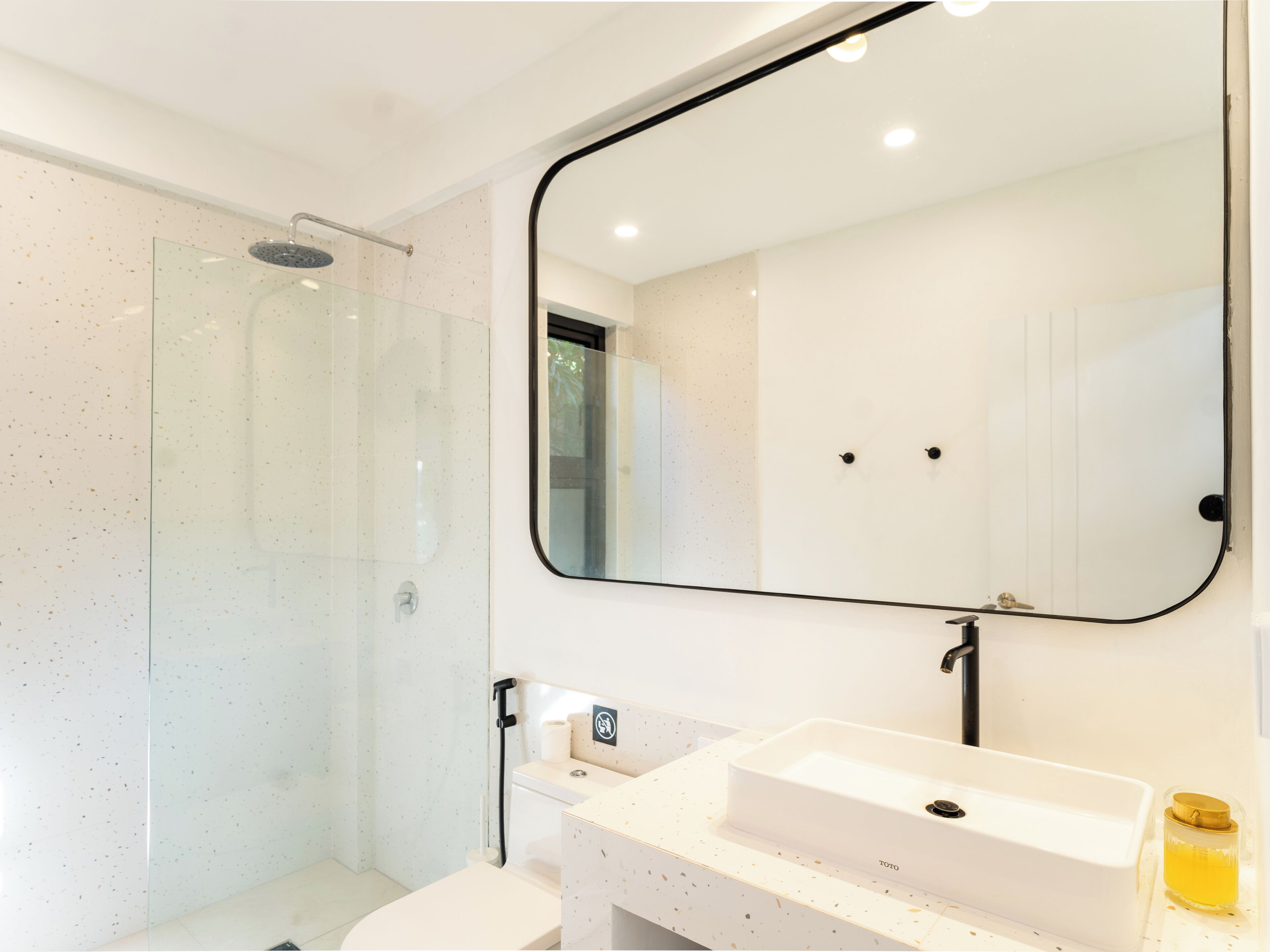 Un baño moderno con cabina de ducha de vidrio, un lavamanos blanco con grifo TOTO y un espejo grande con marco negro.