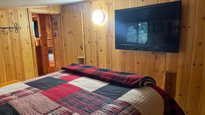 A cozy room with wooden walls, a quilted bedspread, a television mounted on the wall, and a small table.