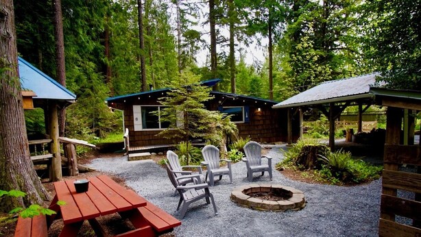 A rustic cabin with a gravel patio, outdoor seating, and a fire pit.