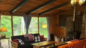 A cozy cabin interior with a wooden ceiling, a stone fireplace, a sofa, a wooden bench, and a table.