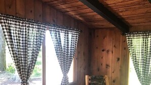 A cabin interior with wooden walls, a wooden dresser, a chair, and checkered curtains.