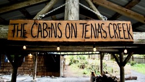 A wooden sign with the text "The Cabins on Texas Creek" hanging under a rustic structure.