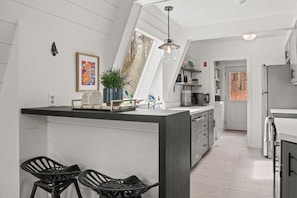 A modern kitchen with a central island, black bar stools, and a large window providing natural light.