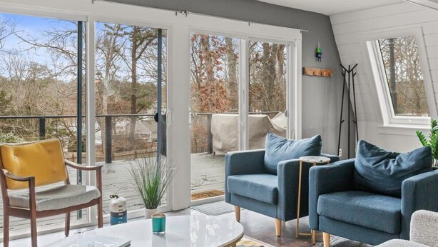 Un salon moderne doté d’une porte vitrée donnant sur une terrasse extérieure, d’un ensemble de canapés, d’une petite table et d’une plante en pot.