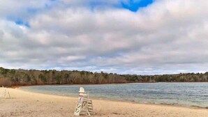 Une plage avec un poste de surveillance pour les sauveteurs et un panneau, des arbres en arrière-plan et un ciel nuageux.