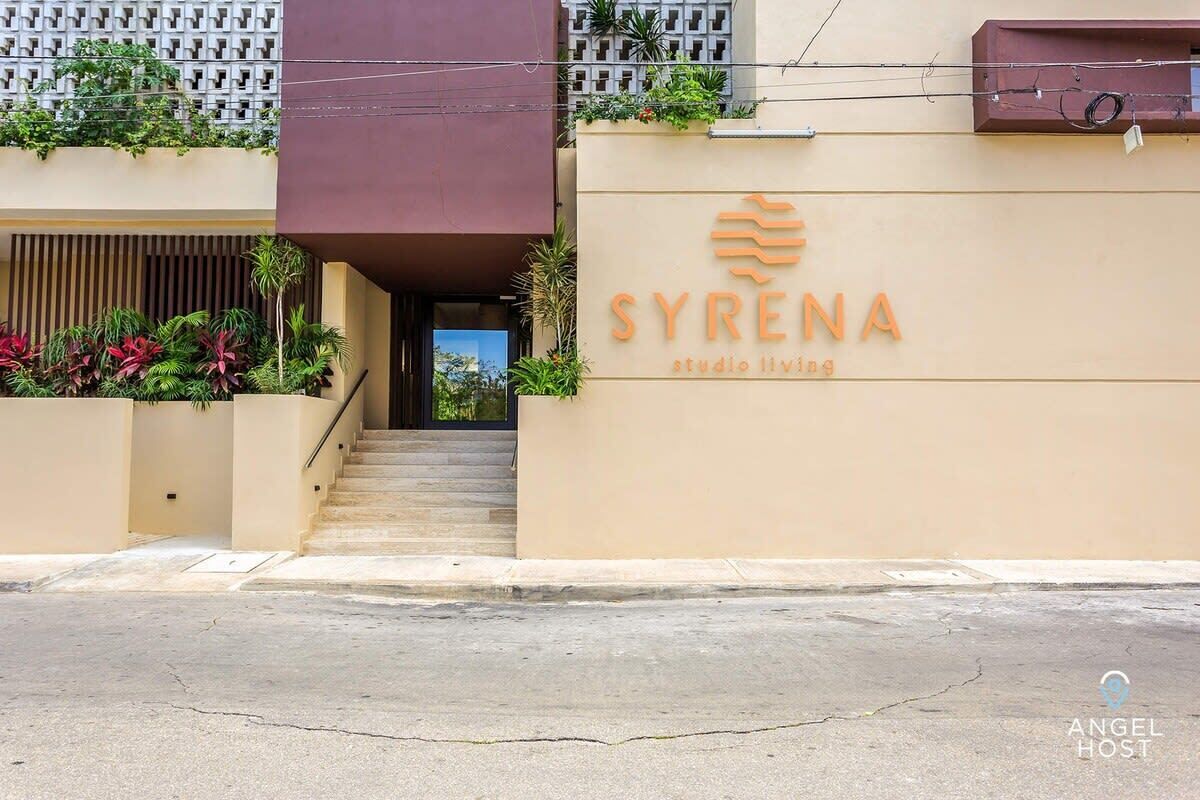 A building with a beige facade, a staircase leading to an entrance, and the name "SYRENA studio living" displayed prominently.
