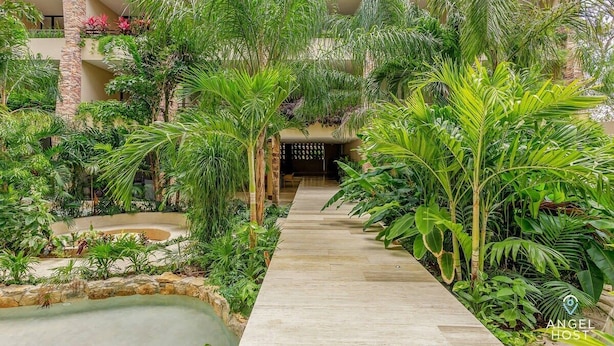 A lush indoor garden with a central pathway leading to a building entrance. - Stylish Playa Condo: Rooftop Pool, Gym, Near Beach (Playa del Carmen)