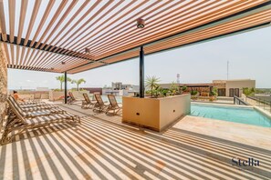 Un espace piscine aménagé sur le toit, avec des chaises longues, une piscine et une vue sur le panorama urbain.