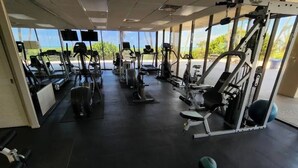 Ein Fitnessstudio mit verschiedenen Trainingsgeräten, großen Fenstern und Blick ins Freie.