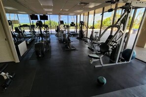 A gym with various exercise machines, large windows, and a view of the outdoors.