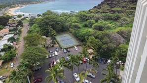 A coastal area with a tennis court, parked cars, and lush greenery.