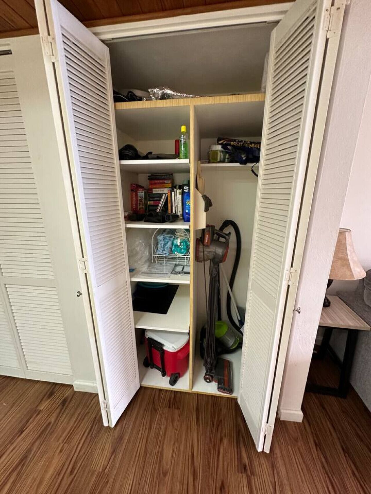 A walk-in closet with shelves, a red storage bin, and a vacuum cleaner.
