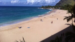 A beach with clear blue water, sandy shore, and a few people.