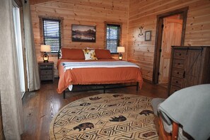 Ein Schlafzimmer in einer Holzhütte mit einem Bett, zwei Nachttischen, einer Kommode und einem gemusterten Teppich.