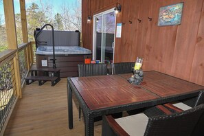 Eine Holzterrasse mit Whirlpool, einem Tisch mit Stühlen und einer Glastür, die in einen Innenbereich führt.