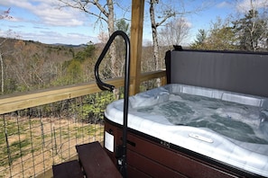 A hot tub on an outdoor deck with a wooden railing, surrounded by a wire fence and trees.