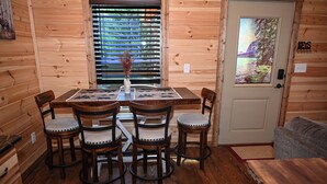 Interior em madeira com mesa de jantar, quatro cadeiras e uma porta com vista panorâmica.