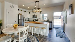 Una cocina moderna con armarios blancos, una isla central con taburetes, un refrigerador de acero inoxidable y un microondas.