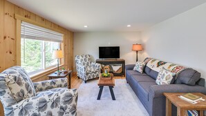A living room with a sofa, armchair, and a television. - Steps to Lake Access! Eastbrook Family Cabin (Eastbrook)