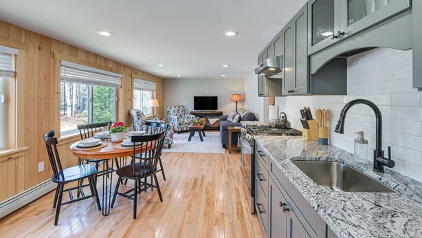 A modern kitchen with a granite countertop, stainless steel sink, and wooden flooring. - Steps to Lake Access! Eastbrook Family Cabin (Eastbrook)