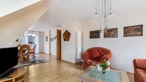 A living room with a TV, sofa, and coffee table, wooden flooring, and a staircase leading to another room. - Apartment 'Ferienwohnung Flensburg Mürwik' with Shared Garden, Balcony and Wi-Fi (Flensburg)