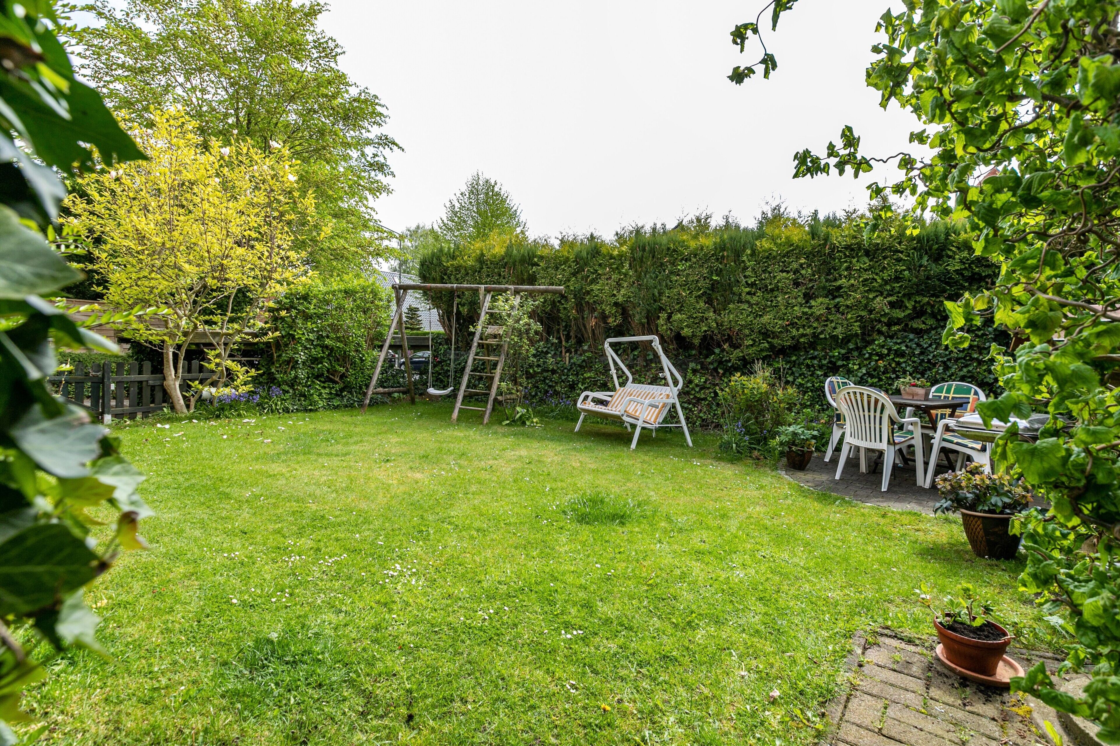A backyard with a swing set, a table with chairs, and a potted plant.