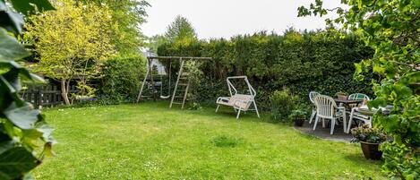 A backyard with a swing set, a table with chairs, and a potted plant.