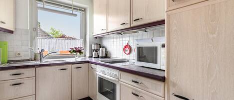 A kitchen with wooden cabinets, a microwave, a stove, and a window with a view of the outside.