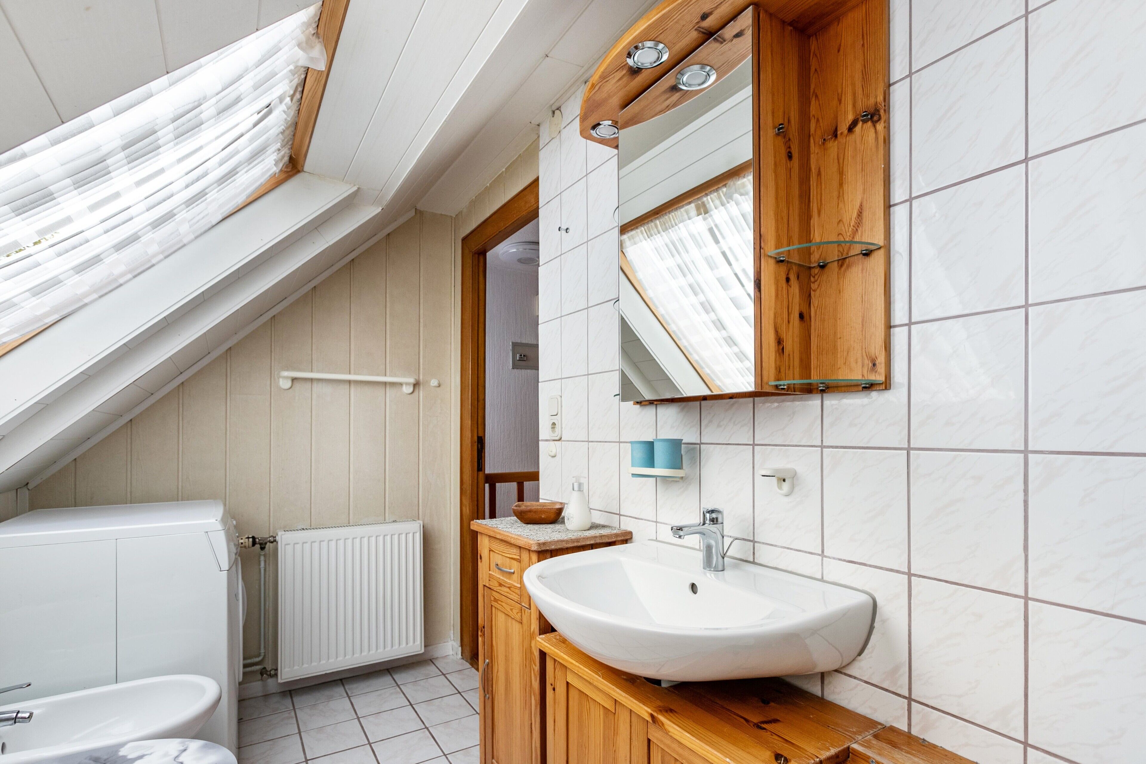 A modern bathroom with a skylight, white tiles, a wooden vanity, and a large mirror.