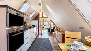 A modern kitchen with a built-in oven, a dining area with a wooden table and chairs, and a view through a skylight. - Holiday Apartment "Dachspitz - Junges Wohnen" with Shared Garden & Wi-Fi (Unterkirnach)