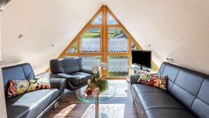 A cozy room with a sloped ceiling, two black leather sofas, a glass coffee table, and a TV on a small table. - Holiday Apartment "Dachspitz - Junges Wohnen" with Shared Garden & Wi-Fi (Unterkirnach)