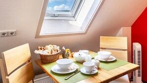 A dining area with a table set for tea, a basket of pastries, and a view through a skylight. - Holiday Apartment "Dachspitz - Junges Wohnen" with Shared Garden & Wi-Fi (Unterkirnach)