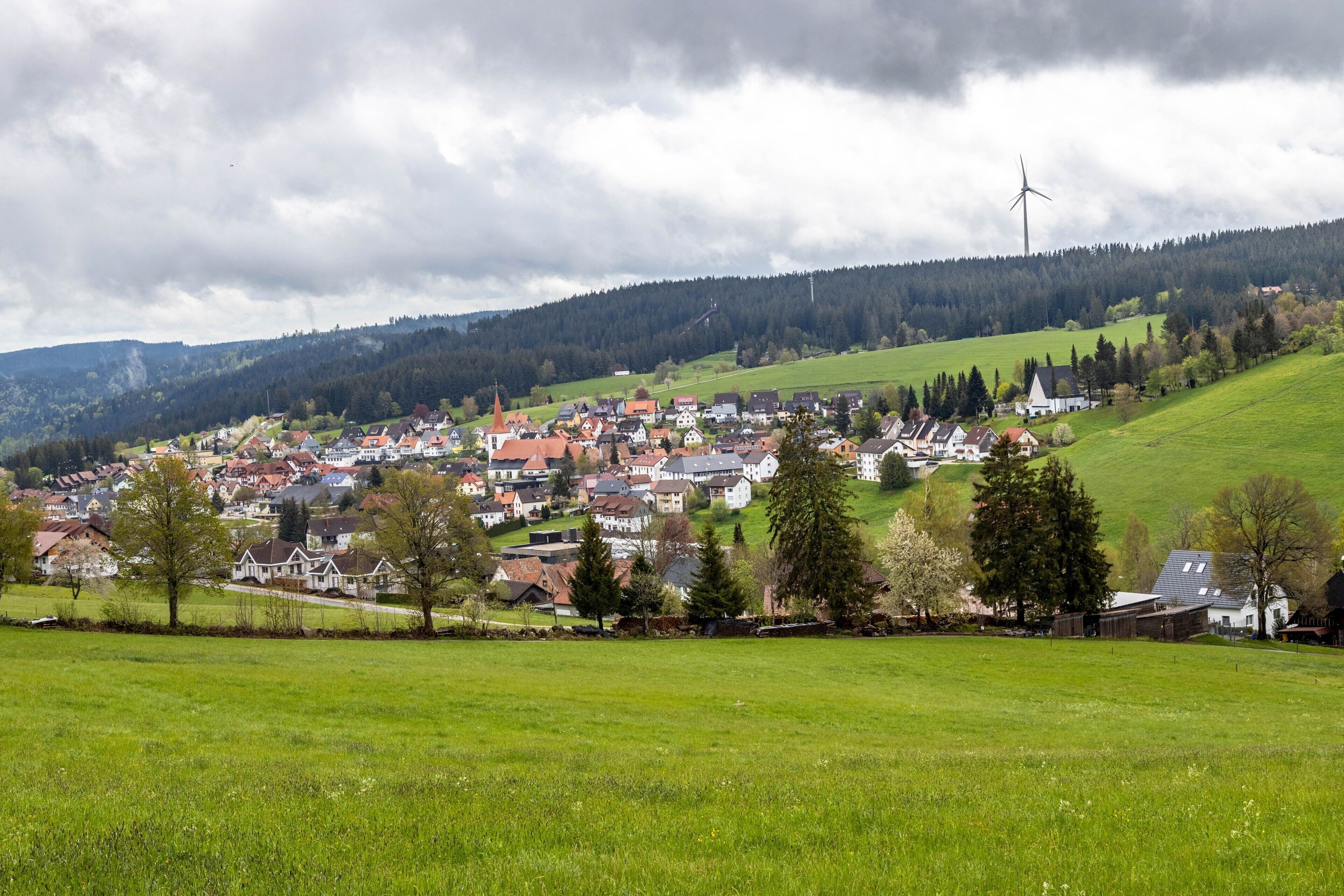 Ein ländliches Dorf mit Häusern, einer Kirche und einer Windkraftanlage.