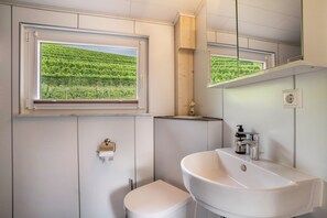 Une salle de bain équipée de toilettes, d’un lavabo, d’un miroir et d’une fenêtre donnant sur un vignoble.