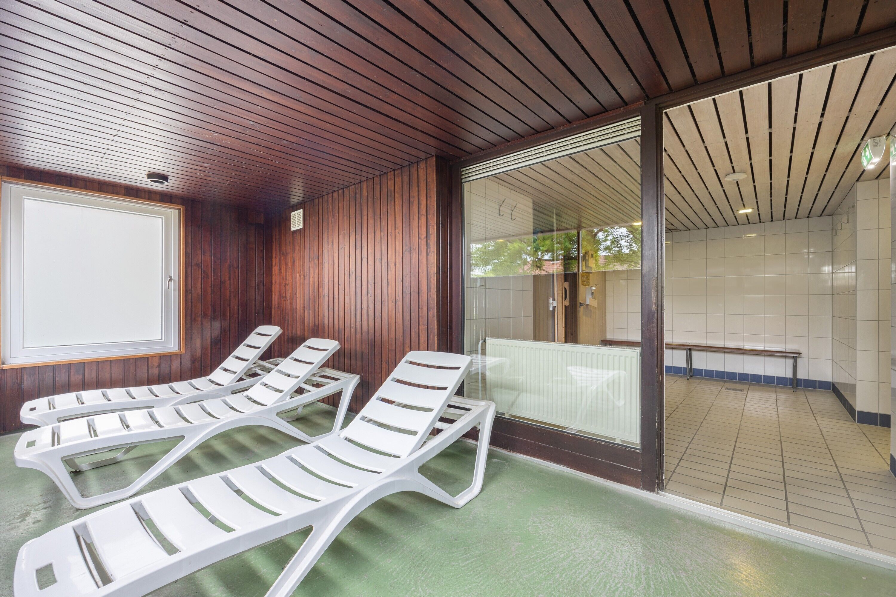 Una habitación con paneles de madera, suelo verde y puerta corredera de vidrio que da a un espacio exterior con una banca.