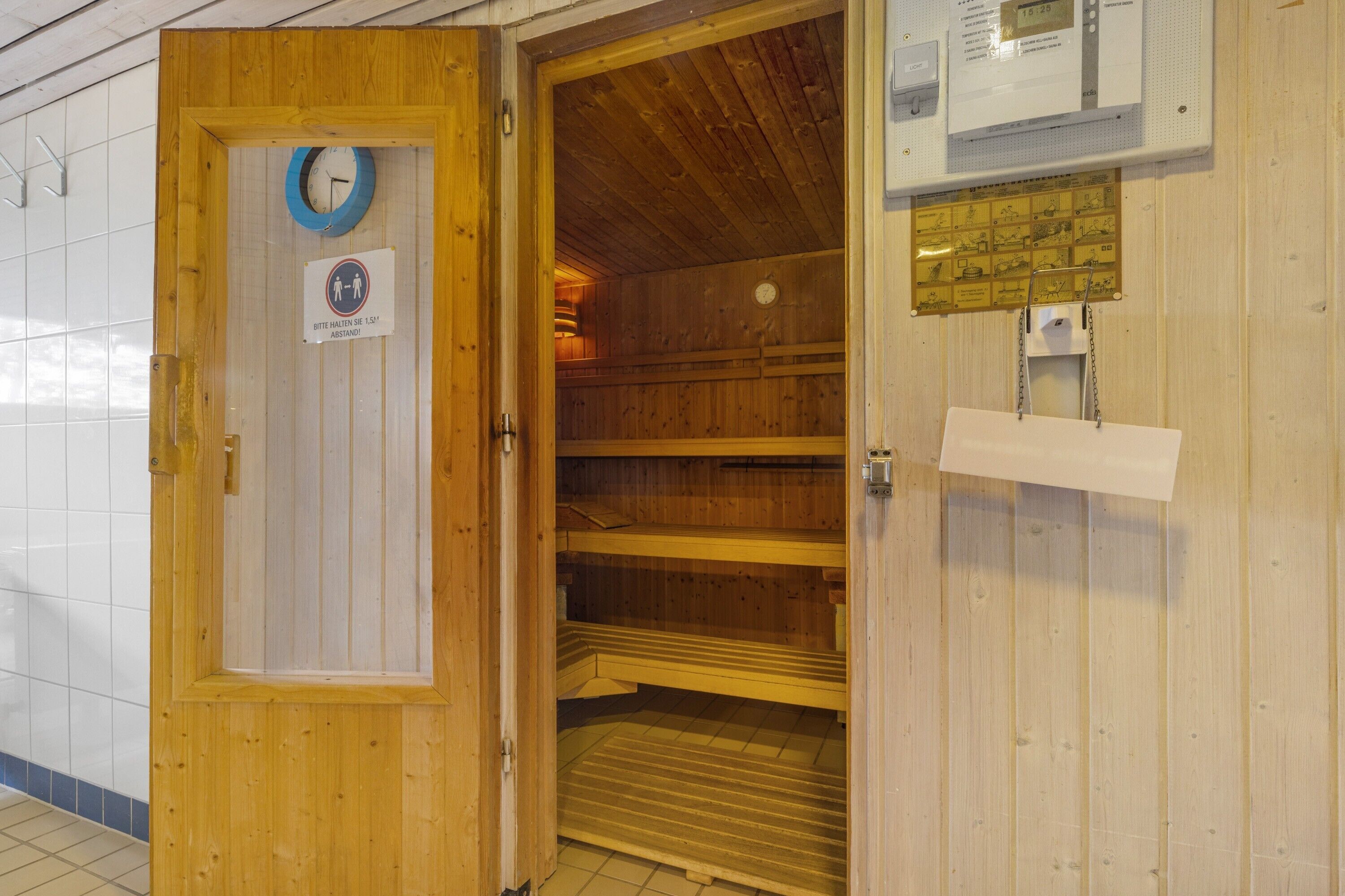Una sala de sauna con paredes y puerta de madera, un reloj y un cartel que indica que la sauna se calienta con agua.